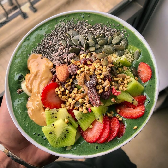 A green smoothie bowl topped with kiwi, strawberries, granola, seeds and peanut butter.